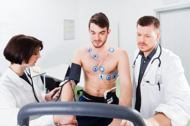 Stress or exercise ECG. A person is connected to electrodes and exercising. The clinician on the left is taking the blood pressure