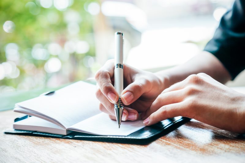 A person holding a pen to write in a journal.